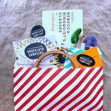 Load image into Gallery viewer, Turn your Colorburst Sampler into a kit with all the supplies you need to get started: embroidery hoop, three colors of embroidery thread, embroidery needle, Creativebug coupon for a free trial, and a Dropcloth Samplers pin.